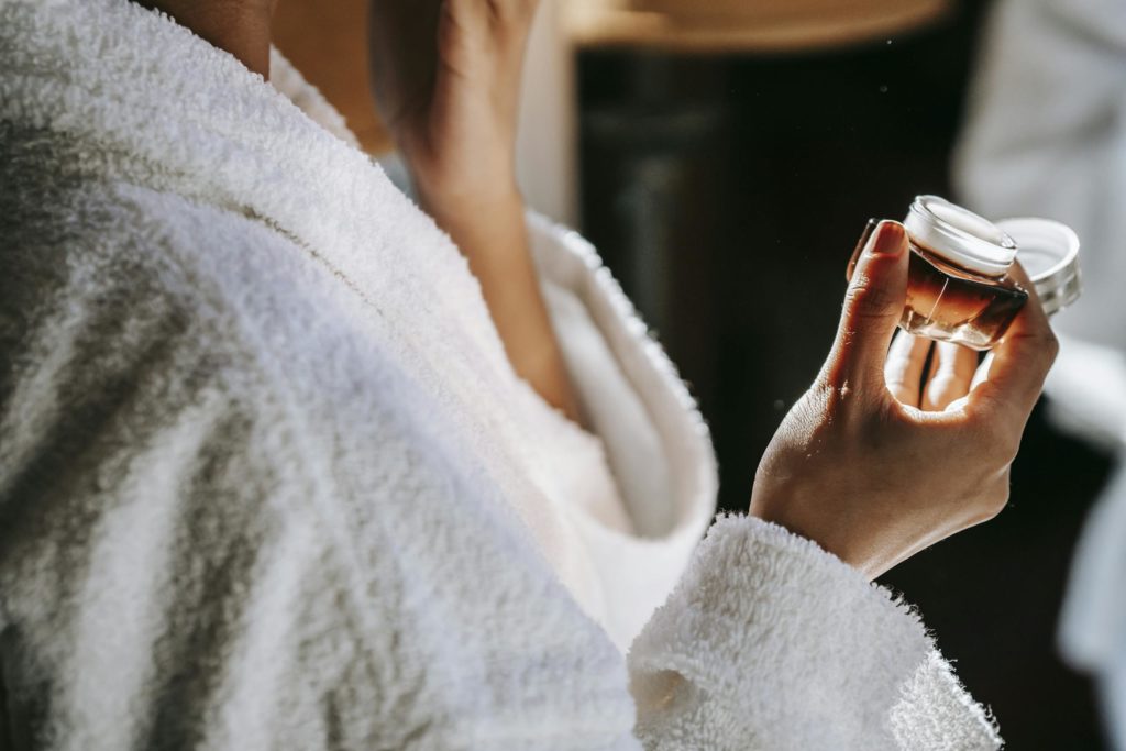 Crop ethnic woman applying nourishing cream on face at home